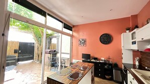 A kitchen with a dining area, a large window, and a clock on the wall. - Arcachon - T4 House Close to the Beach - 6 People (Arcachon)