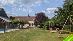 Un patio trasero con piscina, un columpio de madera y una casa de ladrillo al fondo.