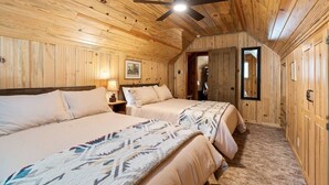 Een slaapkamer in een houten blokhut met twee bedden, een plafondventilator en een deur naar een badkamer.