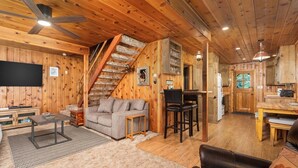 Een gezellig chalet interieur met houten details, een trap, een woonkamer met een bank en een salontafel, en een keukenhoek.