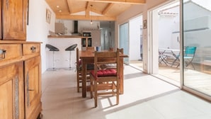 Une cuisine spacieuse avec des poutres en bois, un coin repas avec une table et des chaises, et une porte-fenêtre coulissante donnant sur une terrasse extérieure.