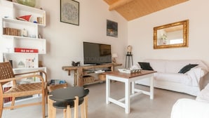 Un salon avec un canapé blanc, une table basse en bois, un téléviseur et une bibliothèque.