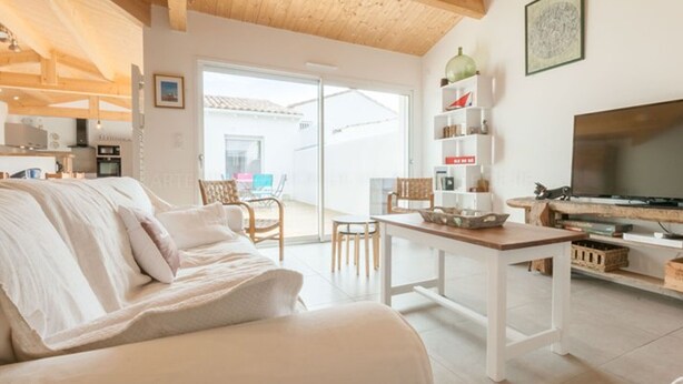 Un salon confortable avec un canapé, une table basse et un téléviseur. Une porte-fenêtre coulissante donne accès à un balcon aménagé avec du mobilier d'extérieur.