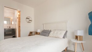 Une chambre à coucher avec un grand lit, des tables de chevet avec des lampes, un miroir rond et une étagère fixée au mur.