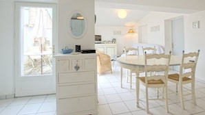 A bright, white room with a dining table and chairs, a dresser with drawers, a mirror, and a door leading to another room. - Apartment with terrace at Ars-en-Ré port, free Wi-Fi (Ars-en-Ré)