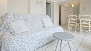 A white sofa with floral upholstery, a small round table, and white chairs in a bright room with white walls and tiled flooring. - Apartment with terrace at Ars-en-Ré port, free Wi-Fi (Ars-en-Ré)