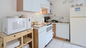 A compact kitchen with white cabinets, a microwave, a stove, and a refrigerator. - Apartment with terrace at Ars-en-Ré port, free Wi-Fi (Ars-en-Ré)