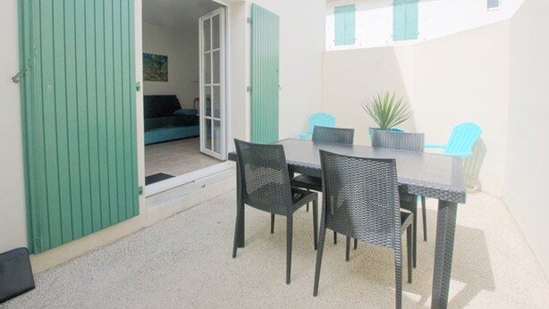 An outdoor patio with a table and chairs, a sliding door, and a view of a building with windows. - Functional ground floor apartment with courtyard and secure garage (Saint-Martin-de-Ré)