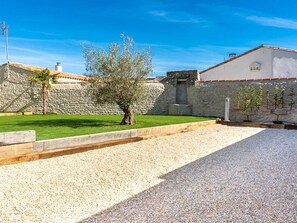 Une cour avec un espace recouvert de gravier, un arbre, des murs en pierre et un bâtiment doté d’un toit en tuiles.