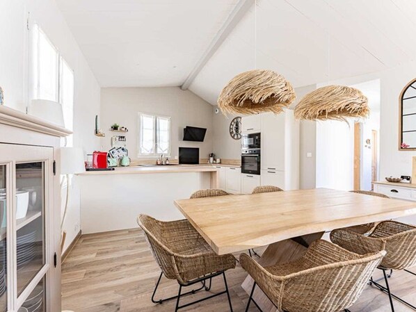 Une cuisine moderne avec des meubles blancs, une table à manger en bois, des chaises en osier et un luminaire suspendu.