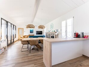 A spacious kitchen with a large island, wooden flooring, and a dining area with wicker chairs.