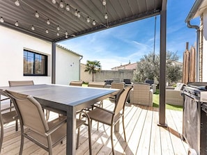 An outdoor patio with a table and chairs, a grill, and a view of the backyard.