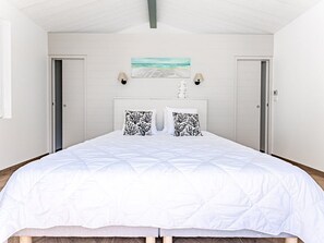 A bedroom with a large bed, two doors, a painting, and a nightstand with a lamp.