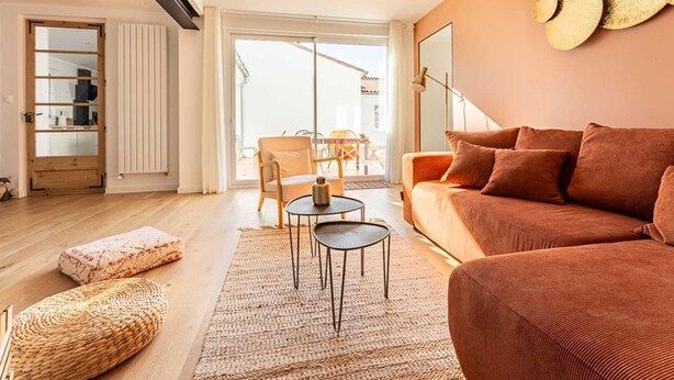 Un salon moderne avec un canapé, une table basse et un fauteuil. Une grande fenêtre laisse entrer la lumière naturelle et offre une vue sur l’extérieur.