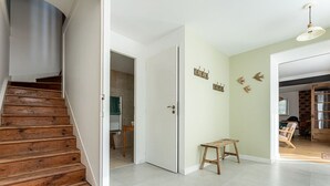 Un escalier menant à une pièce dont le sol est recouvert de carreaux, où se trouve un banc en bois et une porte à laquelle est accrochée une serviette.