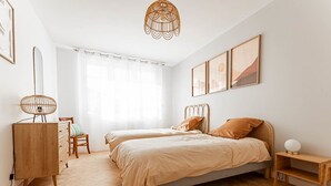 Une chambre moderne avec deux lits, une commode en bois, un bureau et une chaise.