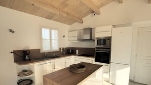 Una cocina moderna con vigas de madera, armarios blancos, una isla central y electrodomésticos integrados.