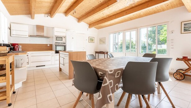 Una cocina moderna con armarios blancos, encimera de madera y un comedor con mesa y sillas.