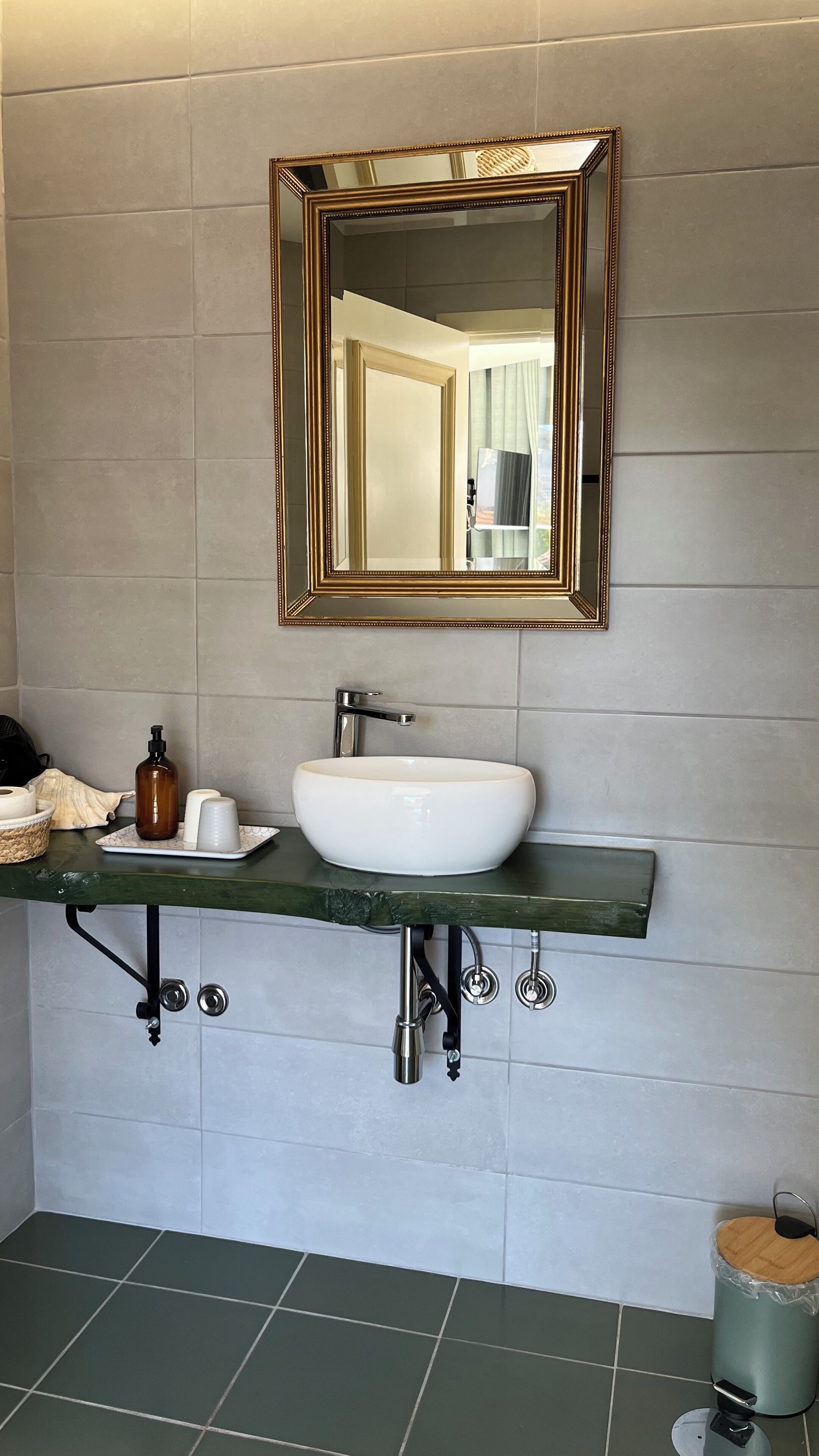 Un bagno con un lavandino bianco, uno specchio con cornice dorata e un piano di lavoro verde.