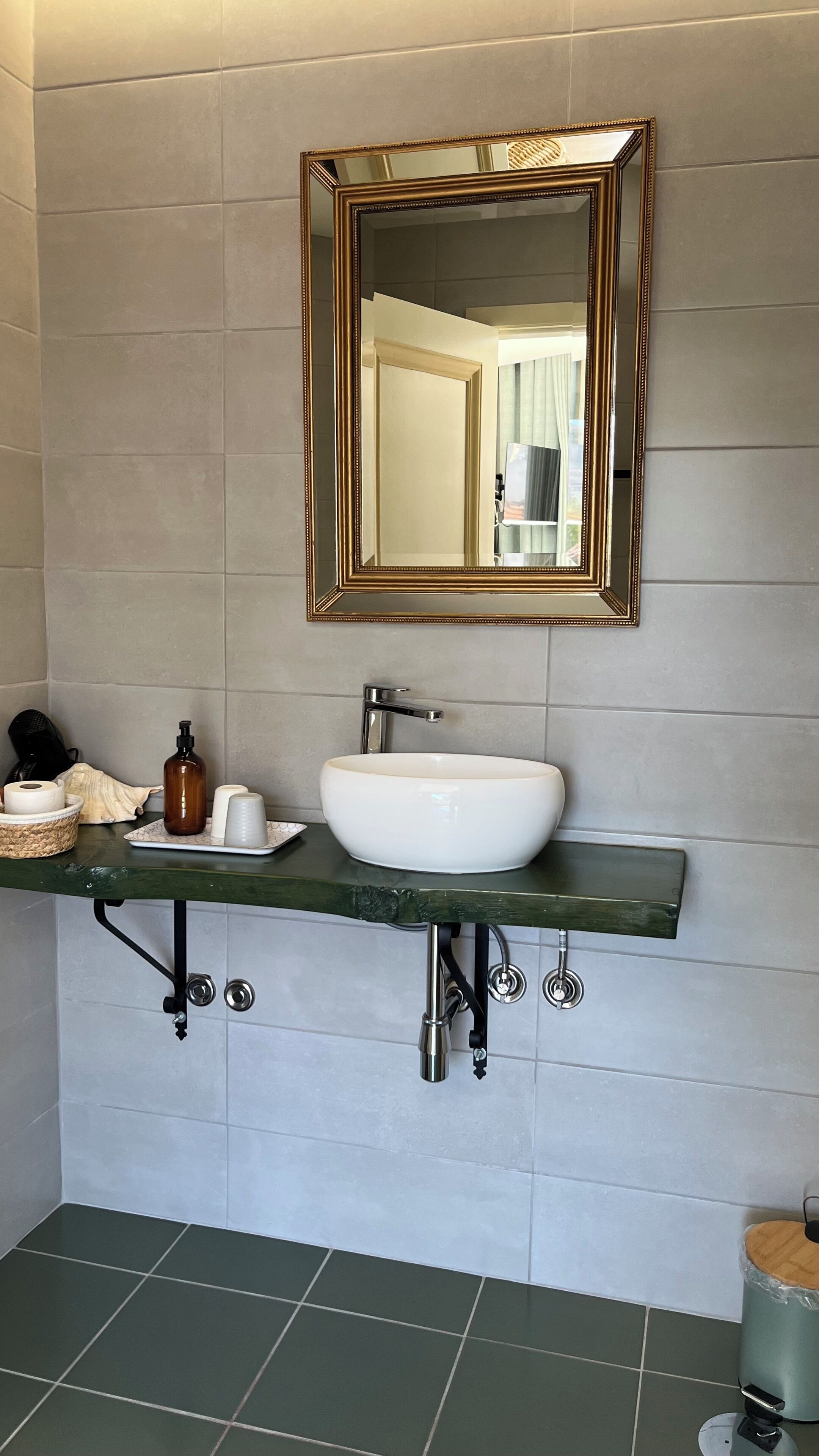 A bathroom with a white sink, a gold-framed mirror, and a green countertop.