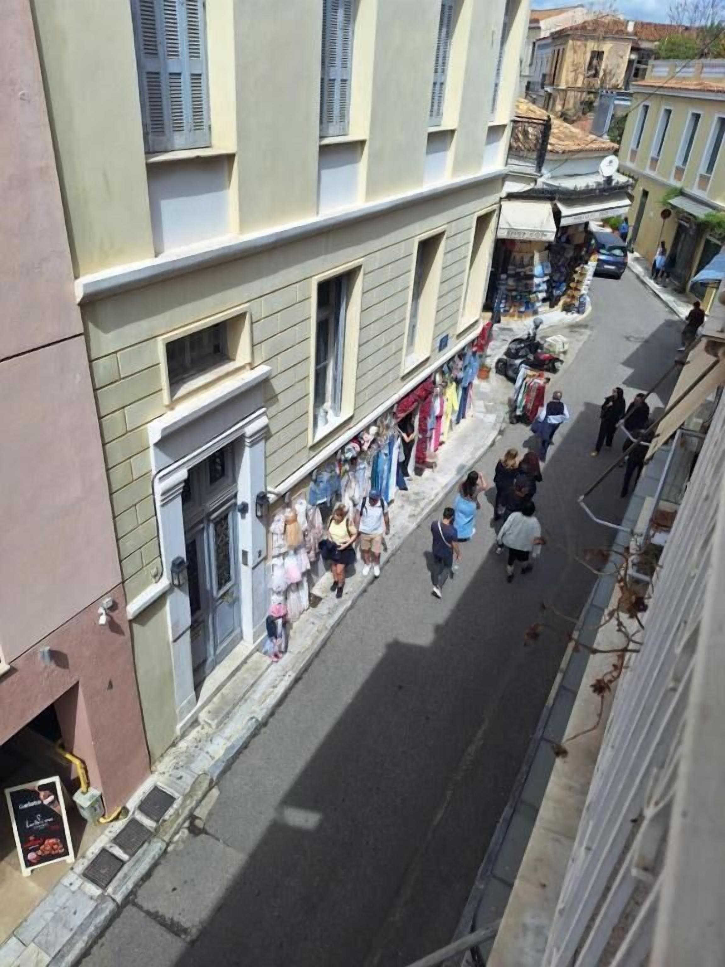 A narrow street with buildings on either side, shops on the ground floor, and people walking.