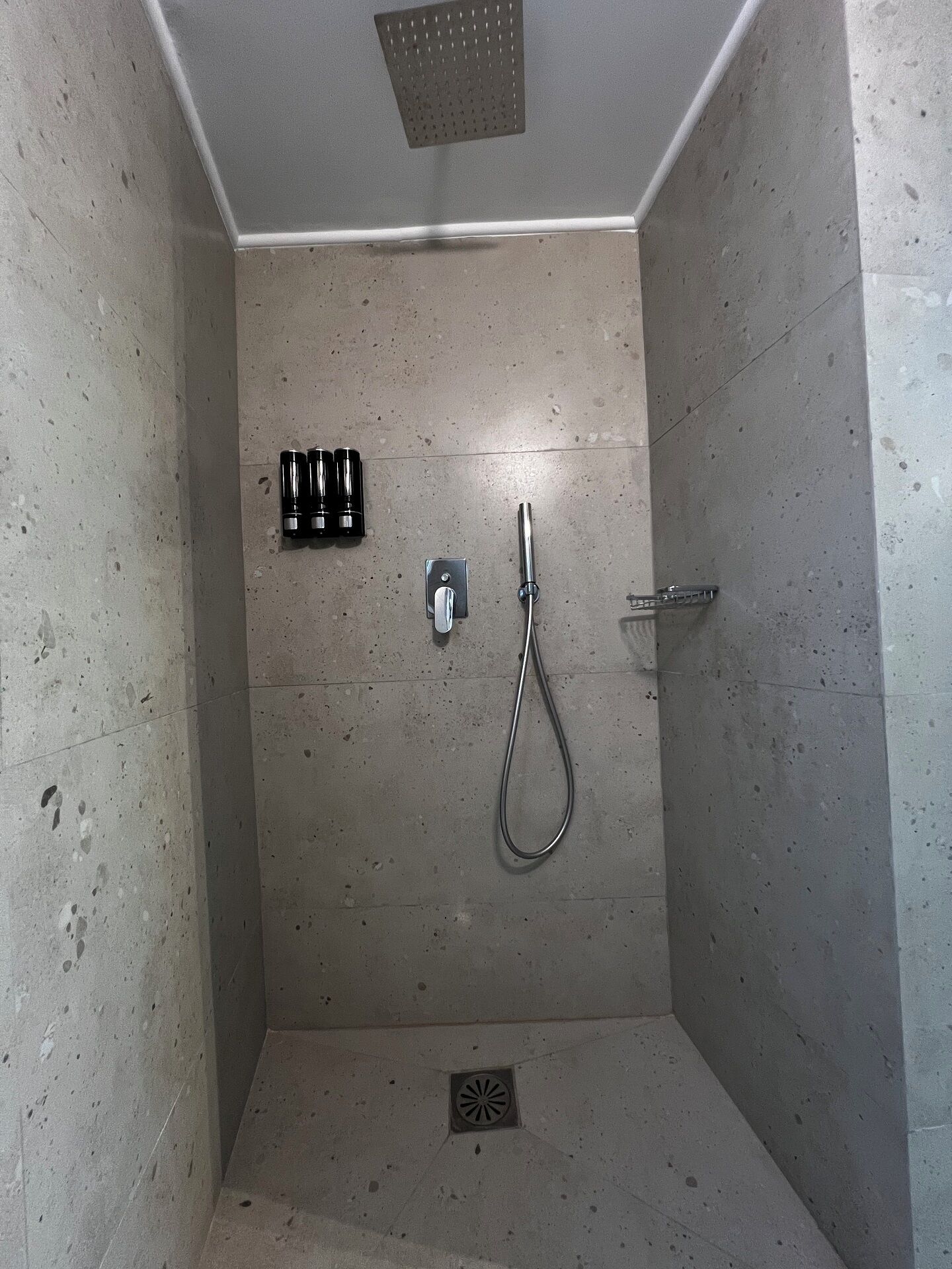 A small, tiled shower room with a handheld showerhead and a wall-mounted faucet.