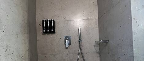 A small, tiled shower room with a handheld showerhead and a wall-mounted faucet.