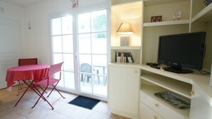 Une pièce comprenant une table à manger et des chaises, un téléviseur posé sur un meuble, et une porte donnant sur un espace extérieur.