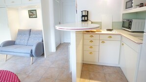 Une cuisine compacte avec des meubles blancs, un four à micro-ondes, une machine à café et un petit coin repas comprenant une chaise et une table.