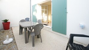 Une petite terrasse avec une table et des chaises, un pot de fleurs et une porte donnant sur un espace intérieur.