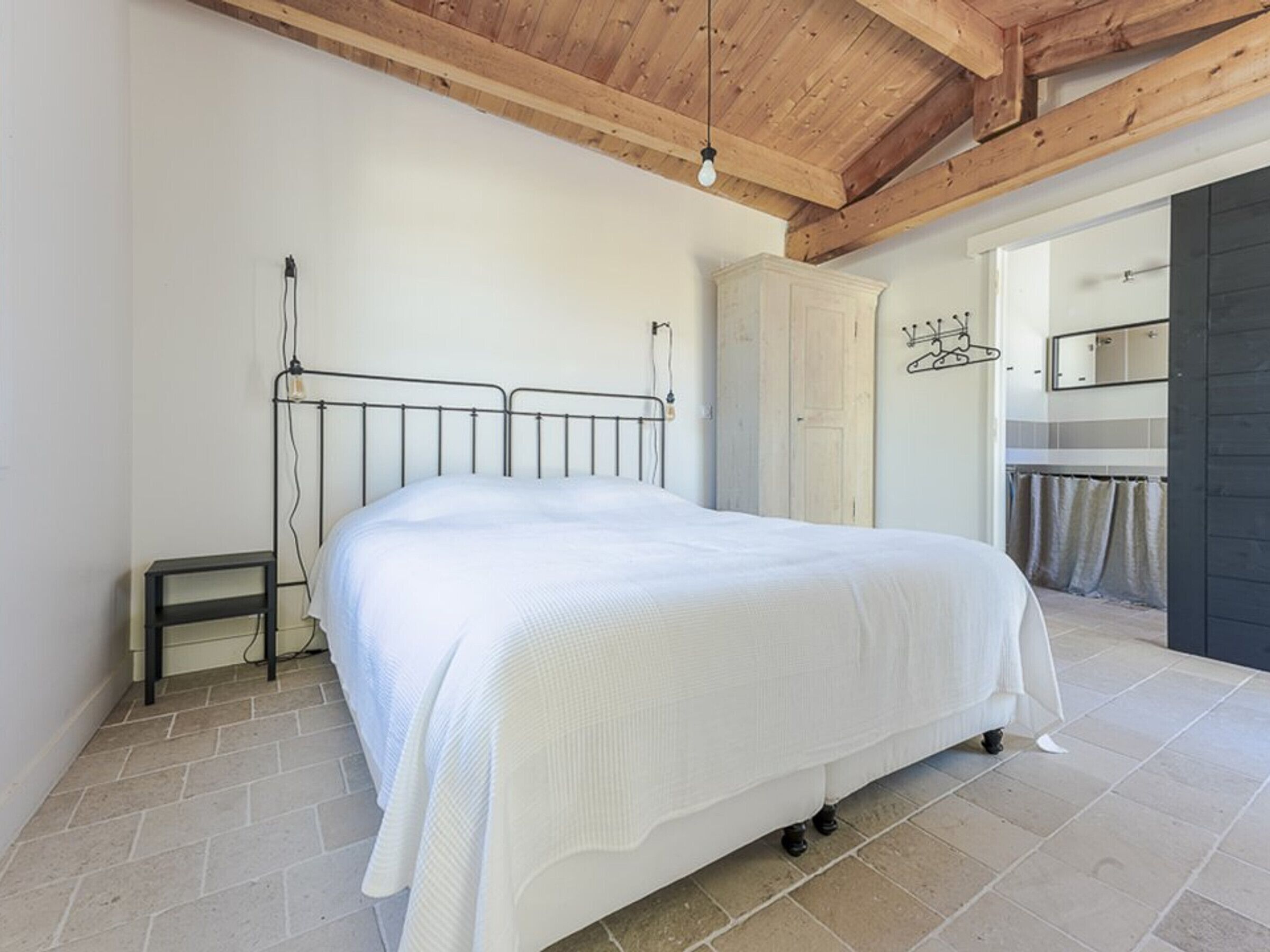 Une chambre à coucher avec un lit, une armoire et une salle de bain visible à travers une porte ouverte.