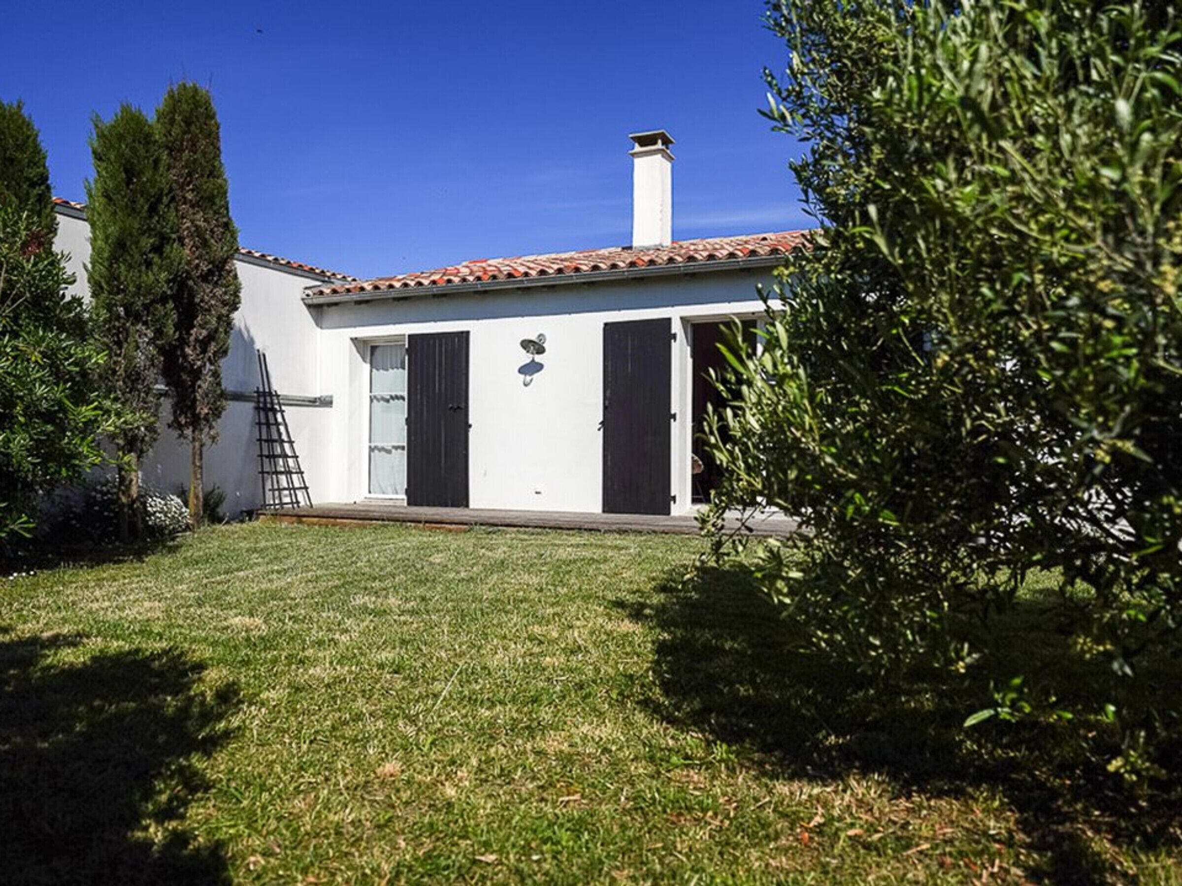 Una casa de un piso con techo de tejas, una chimenea y un pequeño jardín con césped y árboles.