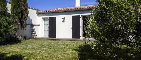 Una casa de un piso con techo de tejas, una chimenea y un pequeño jardín con césped y árboles.