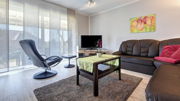 A living room with a sofa, a chair, a coffee table, a TV, and a painting on the wall.