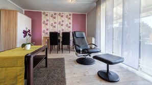 A modern room with a large window, a wooden desk, two chairs, a bench, and a potted orchid.