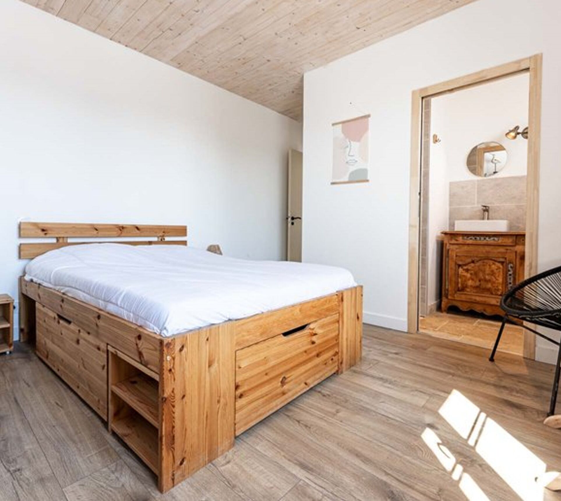 A bedroom with a wooden bed, a nightstand, a dresser, and a bathroom with a sink and mirror.