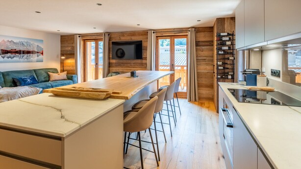 Una cocina moderna con una isla central, taburetes de bar y un espacio para vinos empotrado.