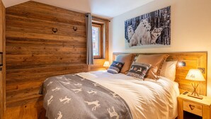 Un dormitorio acogedor con pared de madera, una cama grande con ropa de cama estampada, un cuadro con lobos y una mesita de noche con lámpara.