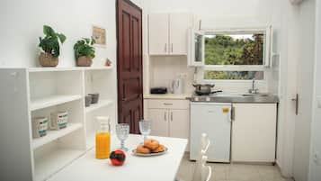 Une cuisine compacte avec des meubles blancs, une petite table à manger et une fenêtre donnant sur un espace verdoyant.