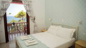 A bedroom with a bed, a nightstand, a bedside table, and a view of the sea through a balcony.