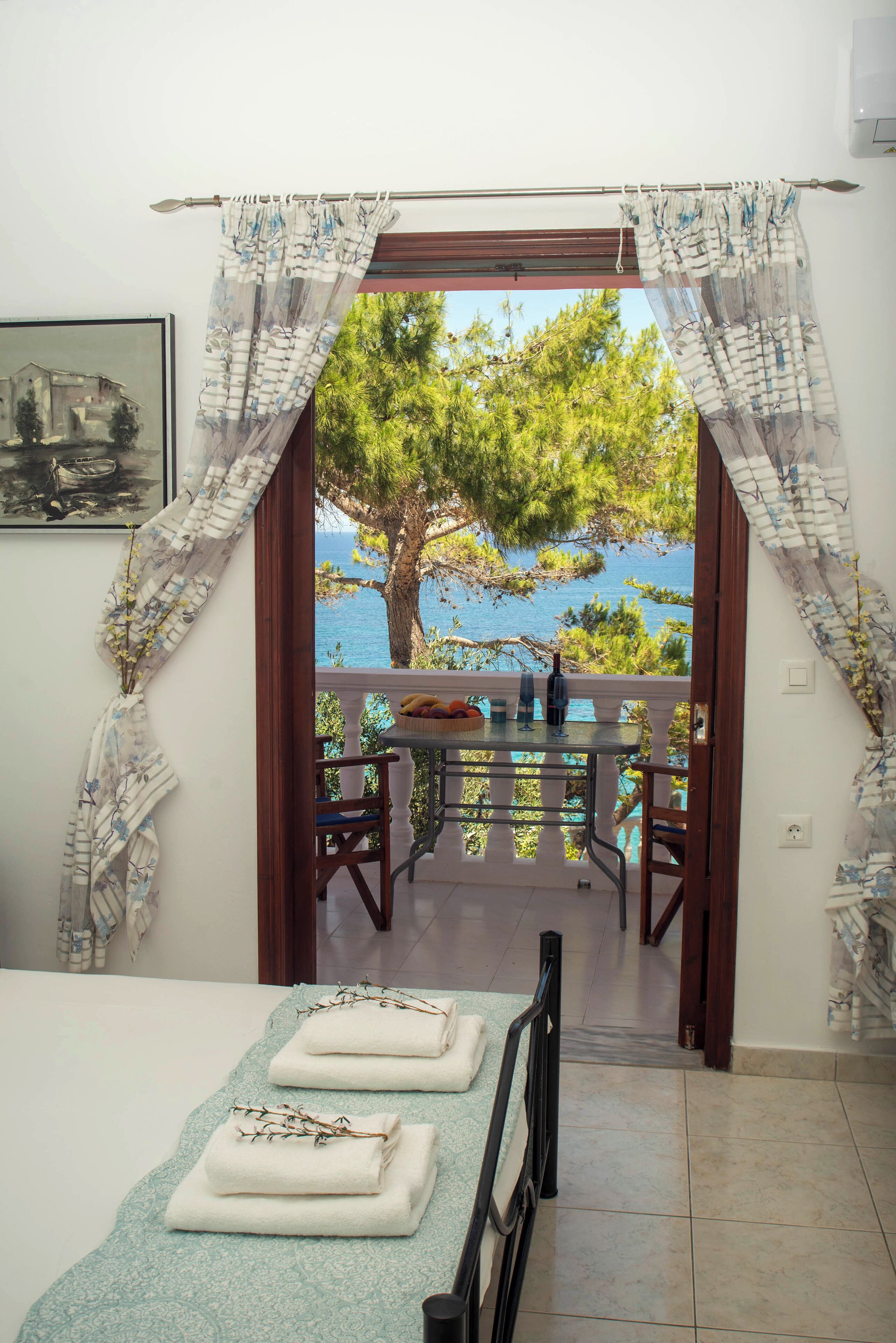 A room with a bed, a table with chairs, and a view of the sea through a window.