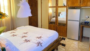 Een slaapkamer met een bed, een houten garderobe, een spiegel en een koelkast.