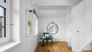 Un pasillo con escalera, una silla verde, una mesita y un espejo redondo en la pared.