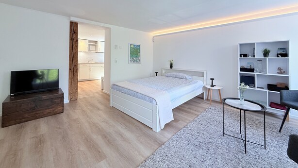 Un dormitorio moderno con cama, televisión, una mesita y una estantería.