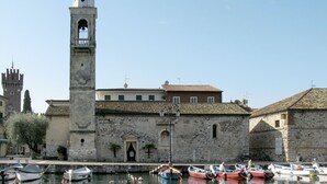 A historic building with a bell tower, stone walls, and a waterfront with boats. - Beautiful apartment for 3 guests with A/C, pool, TV, balcony and pets allowed (Lazise)