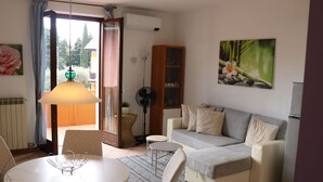 A living room with a sofa, a dining table, and a fan. - Beautiful apartment for 3 guests with A/C, pool, TV, balcony and pets allowed (Lazise)