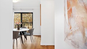 A modern dining area with a round table, grey chairs, and a vase of flowers. - Urban Escape 2BR Wifi Parking (Perth)