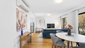 A modern living room with a sofa, TV, and dining area. - Urban Escape 2BR Wifi Parking (Perth)