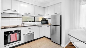 A modern kitchen with white cabinets, a stainless steel refrigerator, a microwave, an oven, and a dishwasher. - Urban Escape 2BR Wifi Parking (Perth)