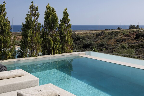 A swimming pool with a view of the sea, surrounded by trees and a hilly landscape.